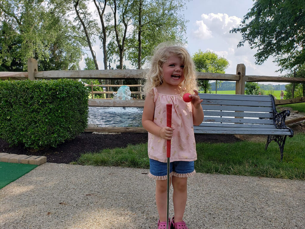 Little girl smiling and holding a mini golf club and ball at Paradise Park in Marion.