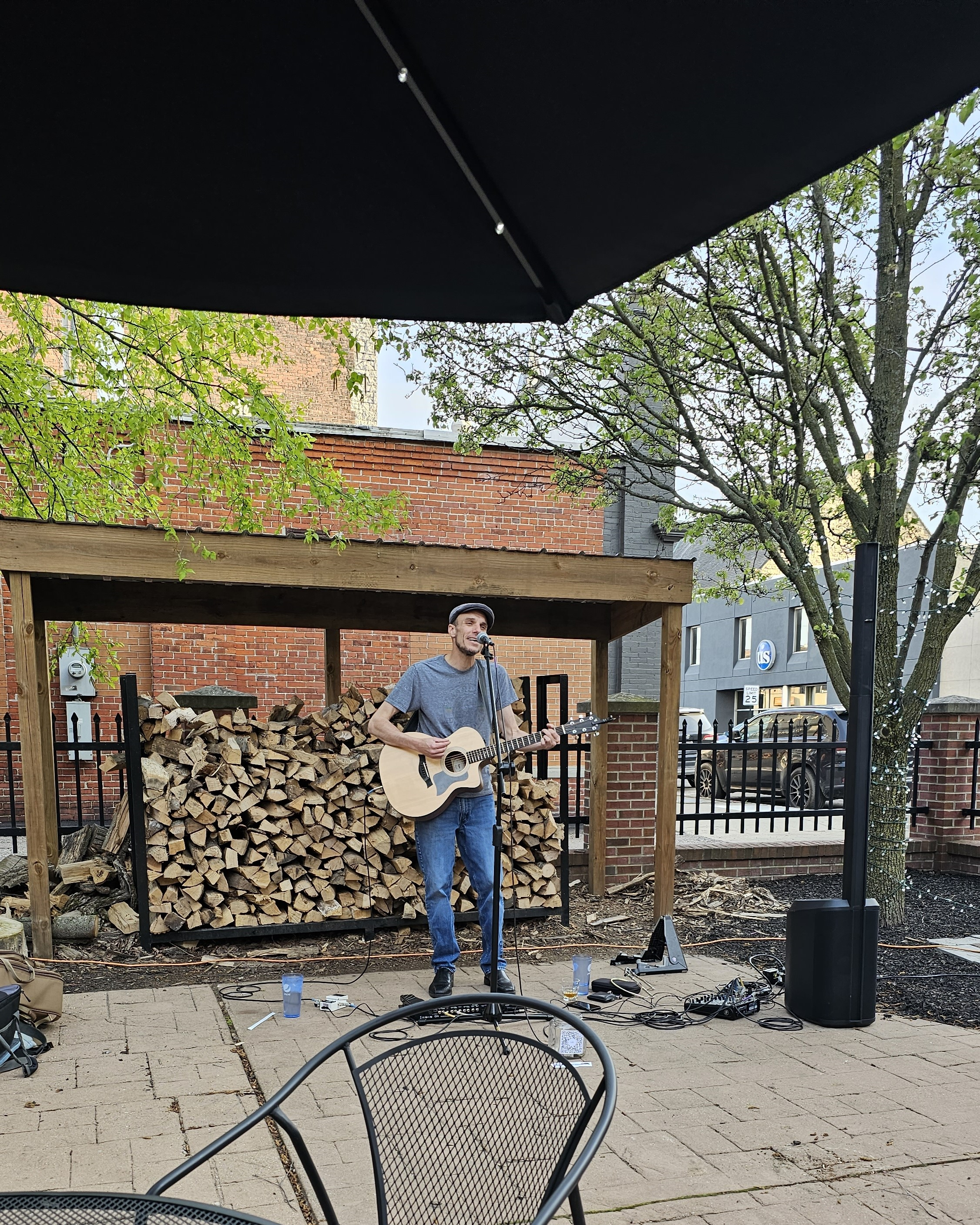 Michael standing with his guitar in front of stacked wood on the Amato's patio
