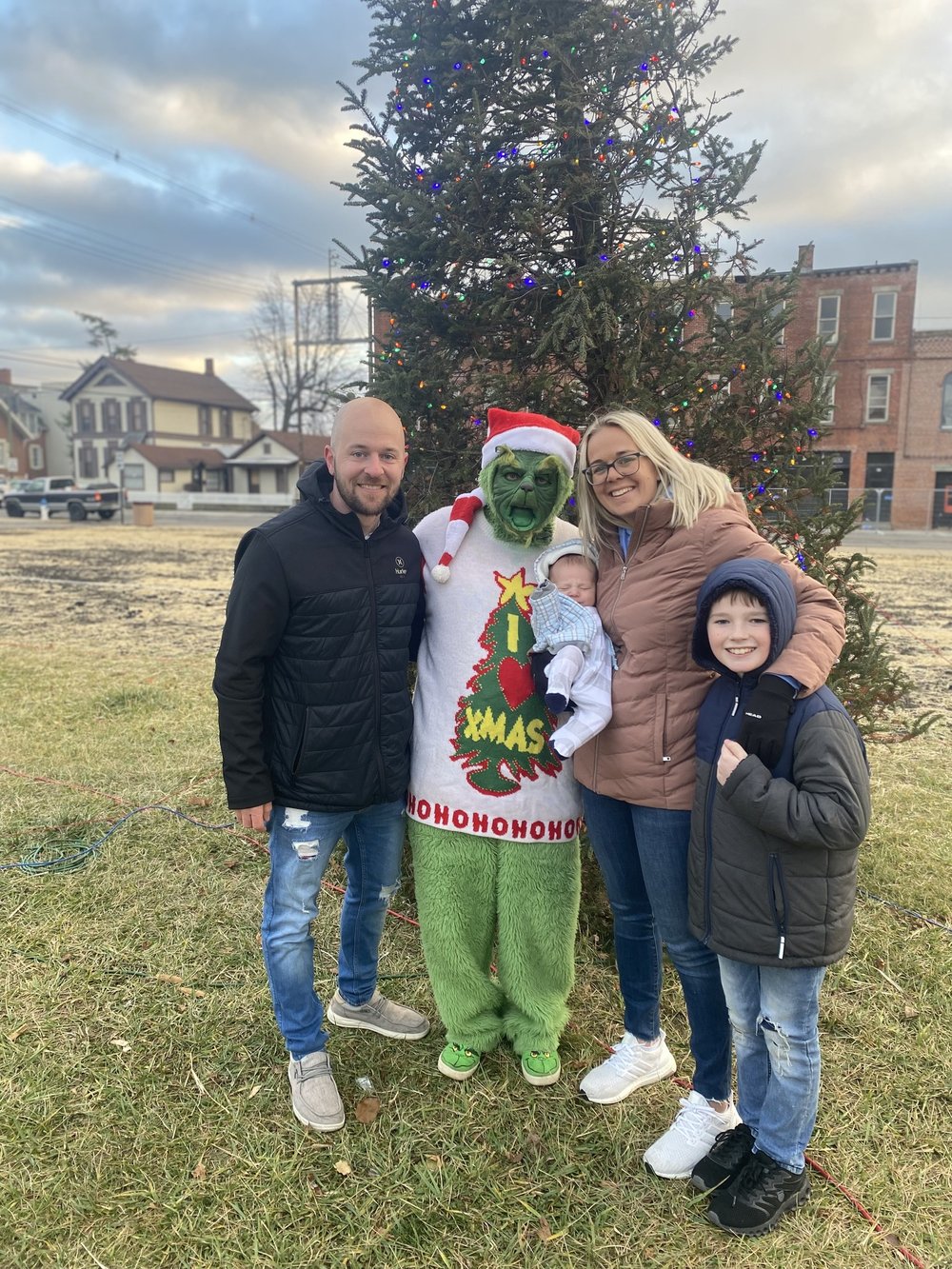 man, woman and 2 kids pose with a green Grinch in a sunny park setting