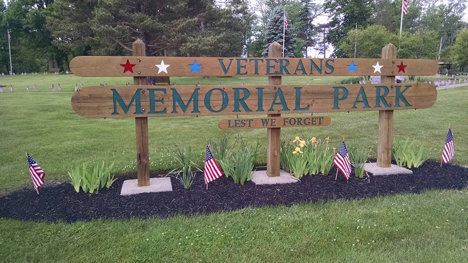 Veterans Memorial Park sign with small flags and flowers